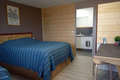 Chambre simple avec un lit double, une table en bois, une chaise et une lumière murale, donnant sur une porte vitrée.