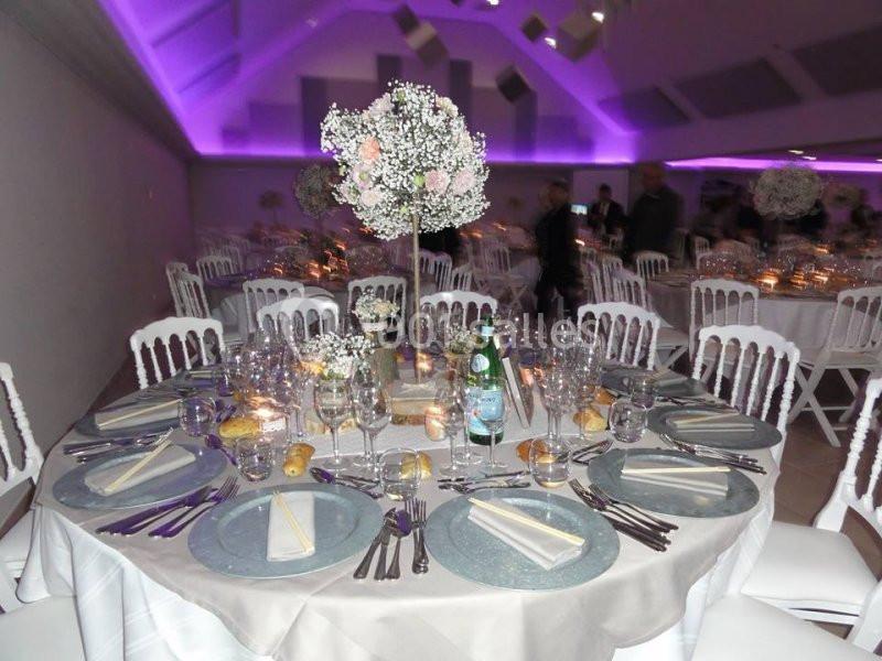 Table de réception élégamment dressée avec vaisselle raffinée, centre de table floral et éclairage violet en arrière-plan.