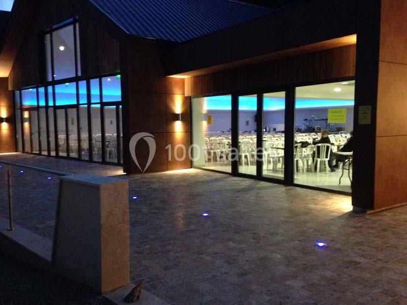 Salle éclairée avec de grandes baies vitrées, vue sur des tables et chaises blanches à l'intérieur, éclairage extérieur…