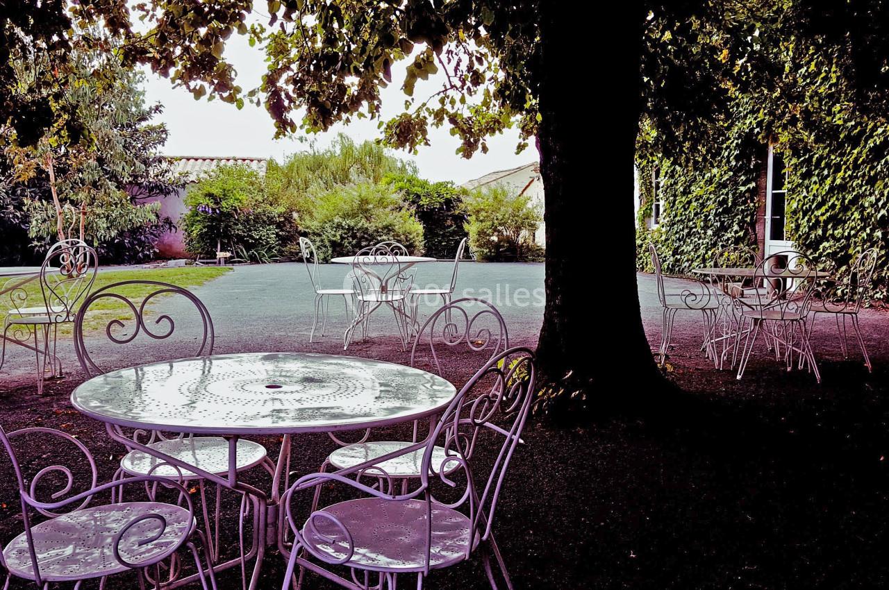 Mobilier de jardin en fer forgé disposé sous des arbres dans une cour ombragée avec un bâtiment couvert de lierre.