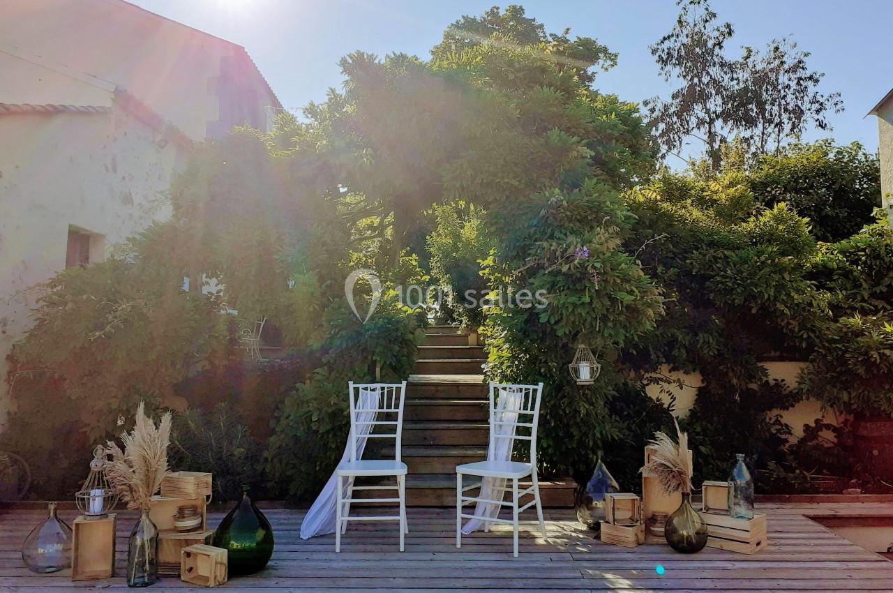 Deux chaises blanches disposées devant un escalier en bois entouré de verdure, avec des décorations naturelles.