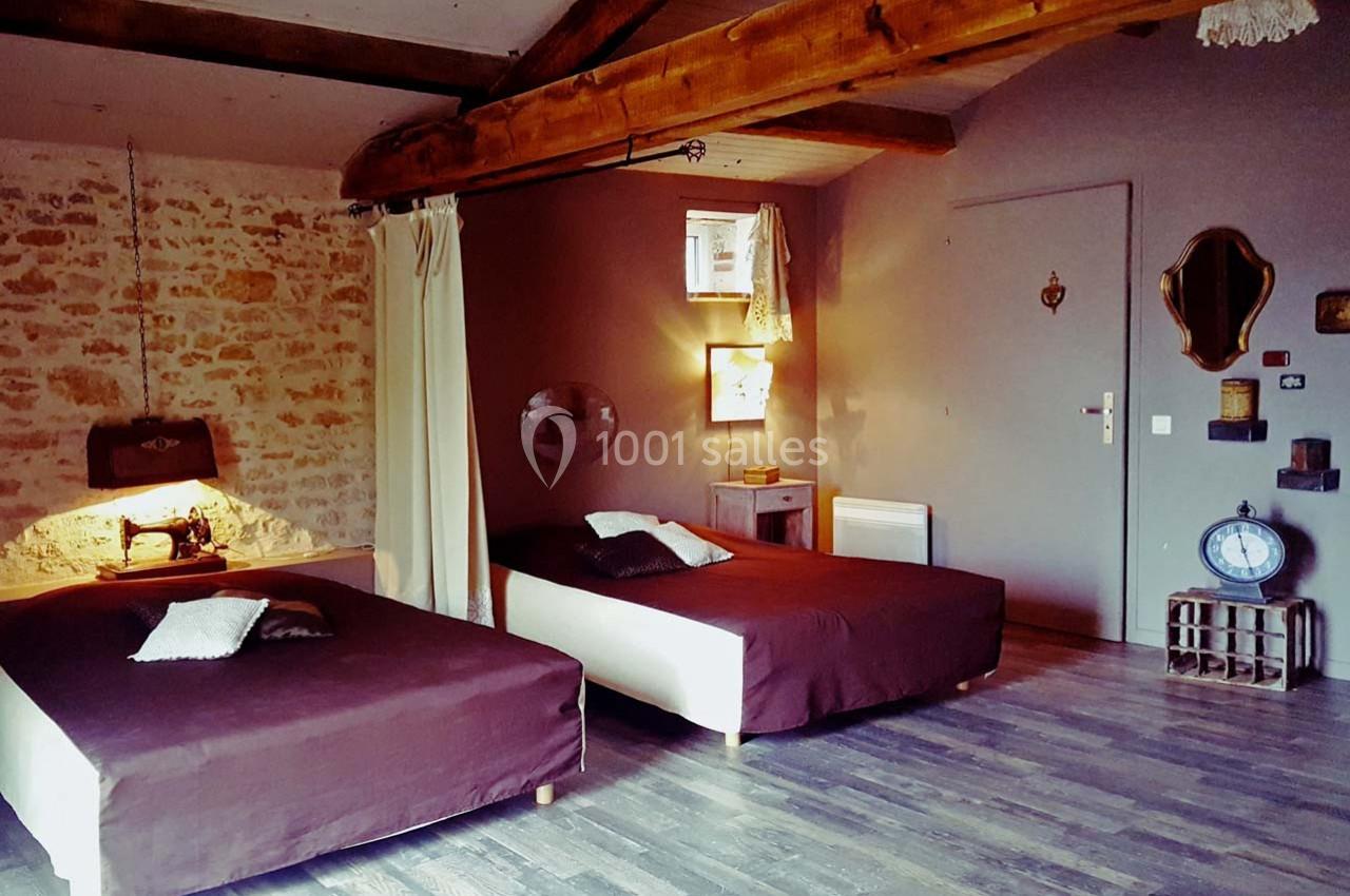 Chambre avec deux lits simples, murs en pierre et bois, éclairage chaleureux et décoration rustique.