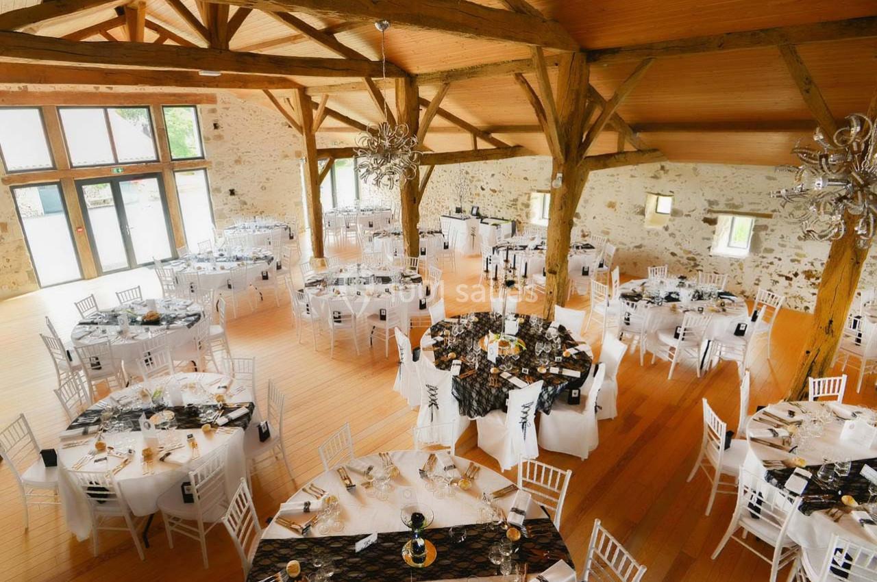 Salle de réception lumineuse avec des tables rondes décorées de nappes noires et blanches, entourées de chaises blanches.