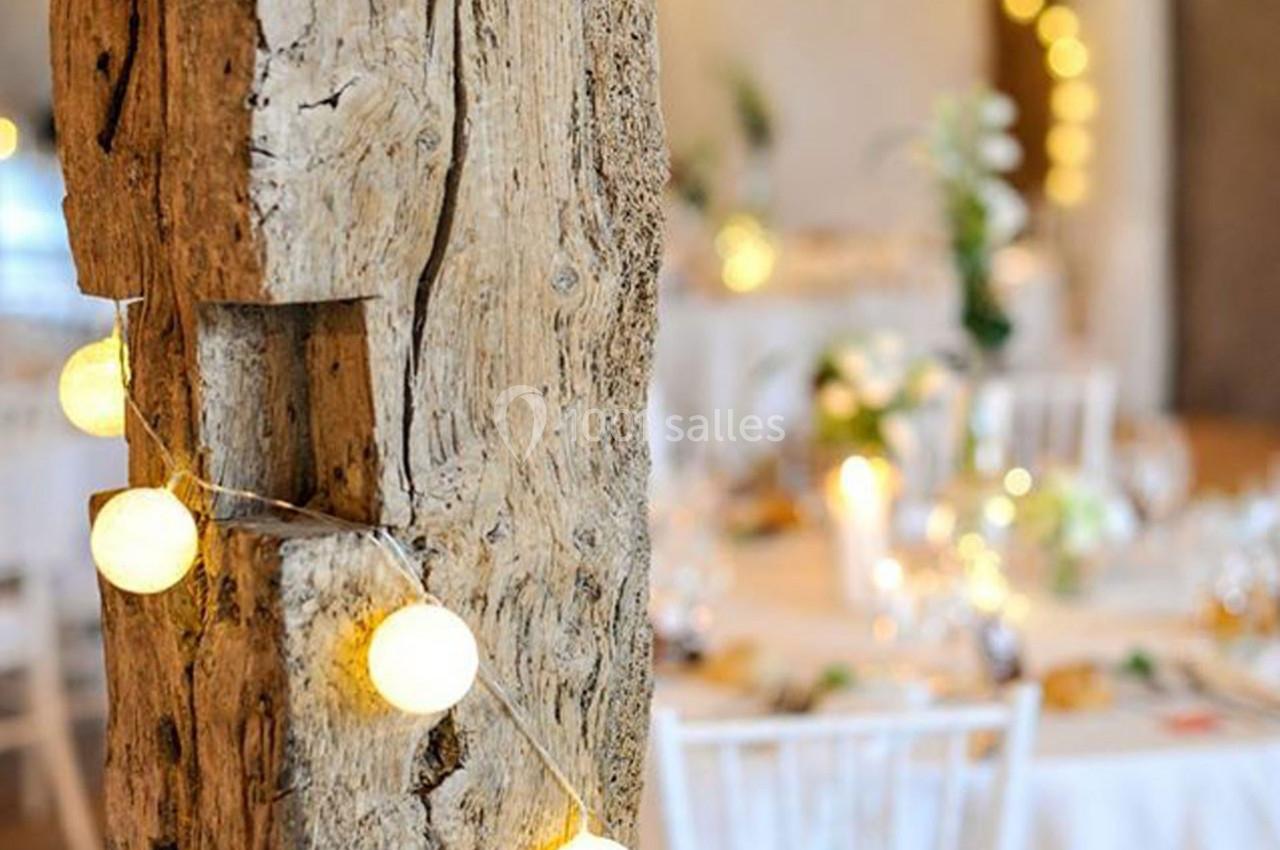 Guirlande lumineuse suspendue à une poutre en bois, avec des tables décorées en arrière-plan flou.