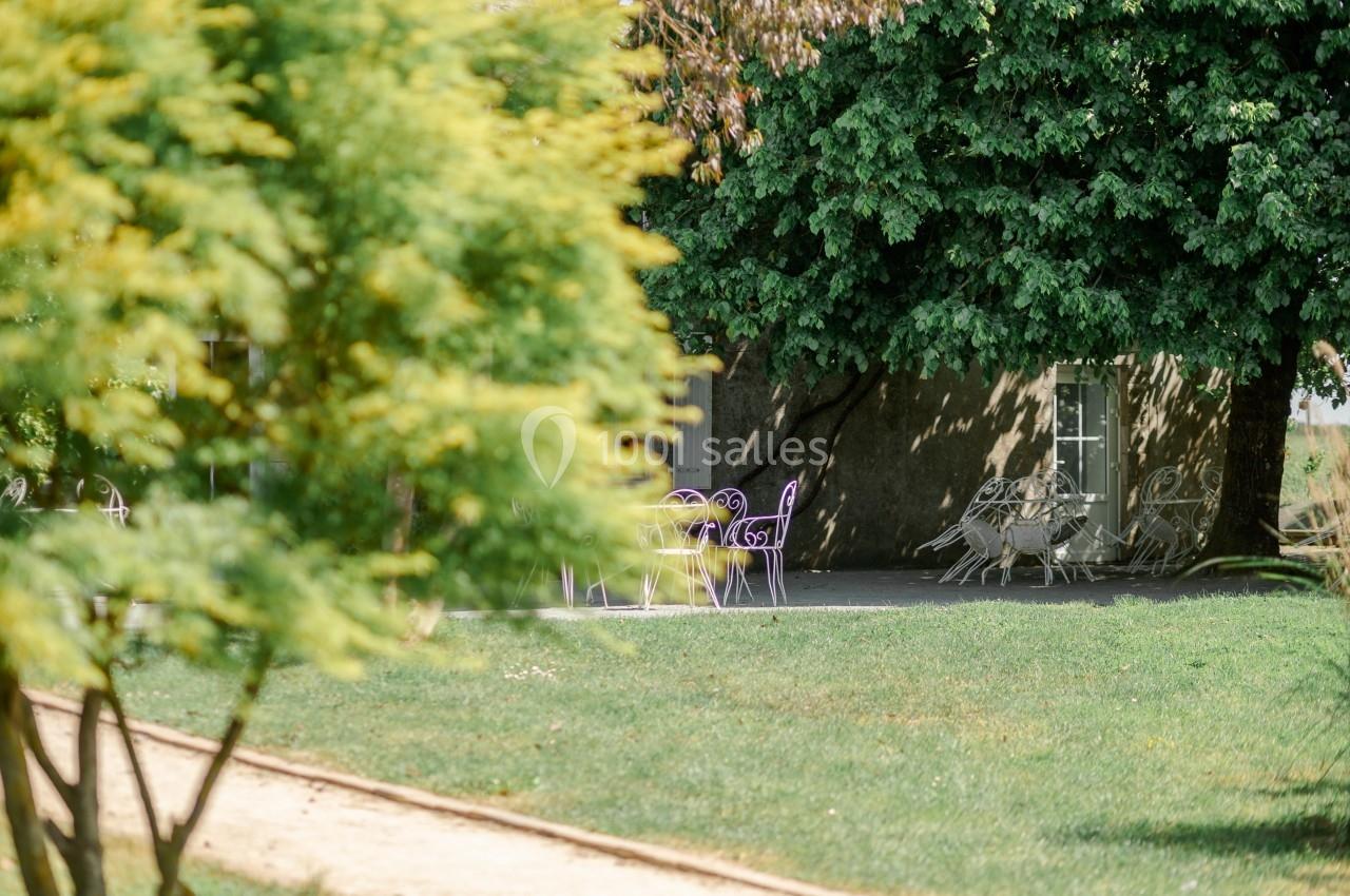 Chaises et tables en métal violet et blanc disposées sous des arbres dans un jardin verdoyant.