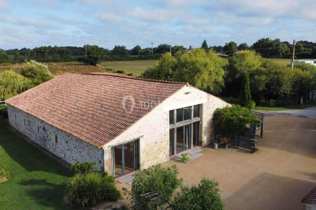 Vue aérienne d'un bâtiment en pierre avec toit en tuiles, entouré de végétation et situé dans un cadre rural.