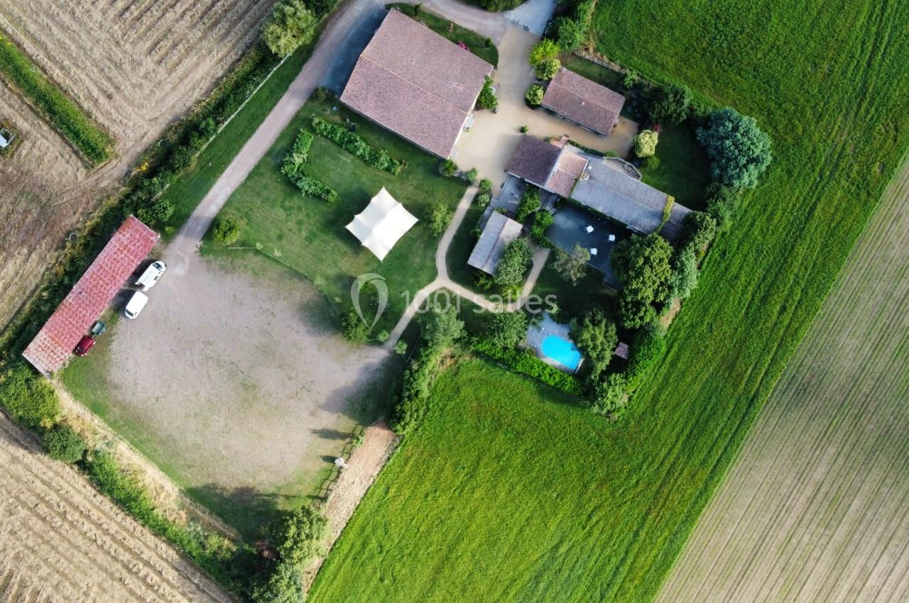 Vue aérienne d'une propriété rurale avec plusieurs bâtiments, une piscine, une tente blanche et des champs environnants.