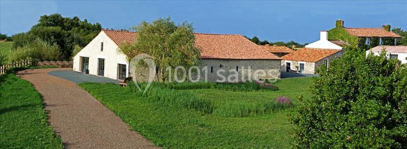 Bâtiments en pierre avec toits en tuiles rouges entourés de verdure et d'un chemin de gravier sous un ciel dégagé.