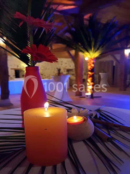 Bougies allumées sur une table décorée de feuilles et de fleurs, dans une salle éclairée aux tons chaleureux.