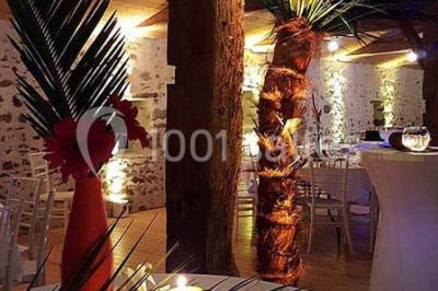 Espace salon lumineux avec fauteuils en osier, cheminée en pierre, piano, plantes et fenêtre donnant sur un jardin.