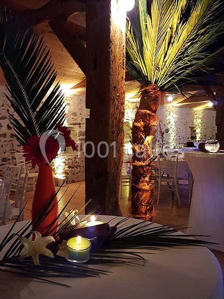 Décoration tropicale avec feuilles de palmier, bougies et fleurs rouges sur une table dans une salle éclairée.
