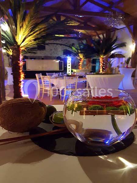 Décoration tropicale avec un vase contenant une fleur rouge, un citron vert et une noix de coco en premier plan.