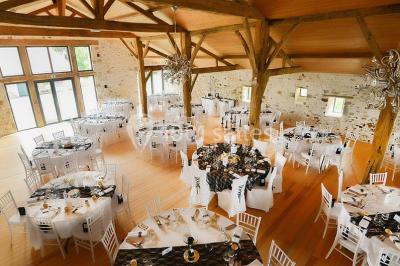 Espace salon lumineux avec fauteuils en osier, cheminée en pierre, piano, plantes et fenêtre donnant sur un jardin.