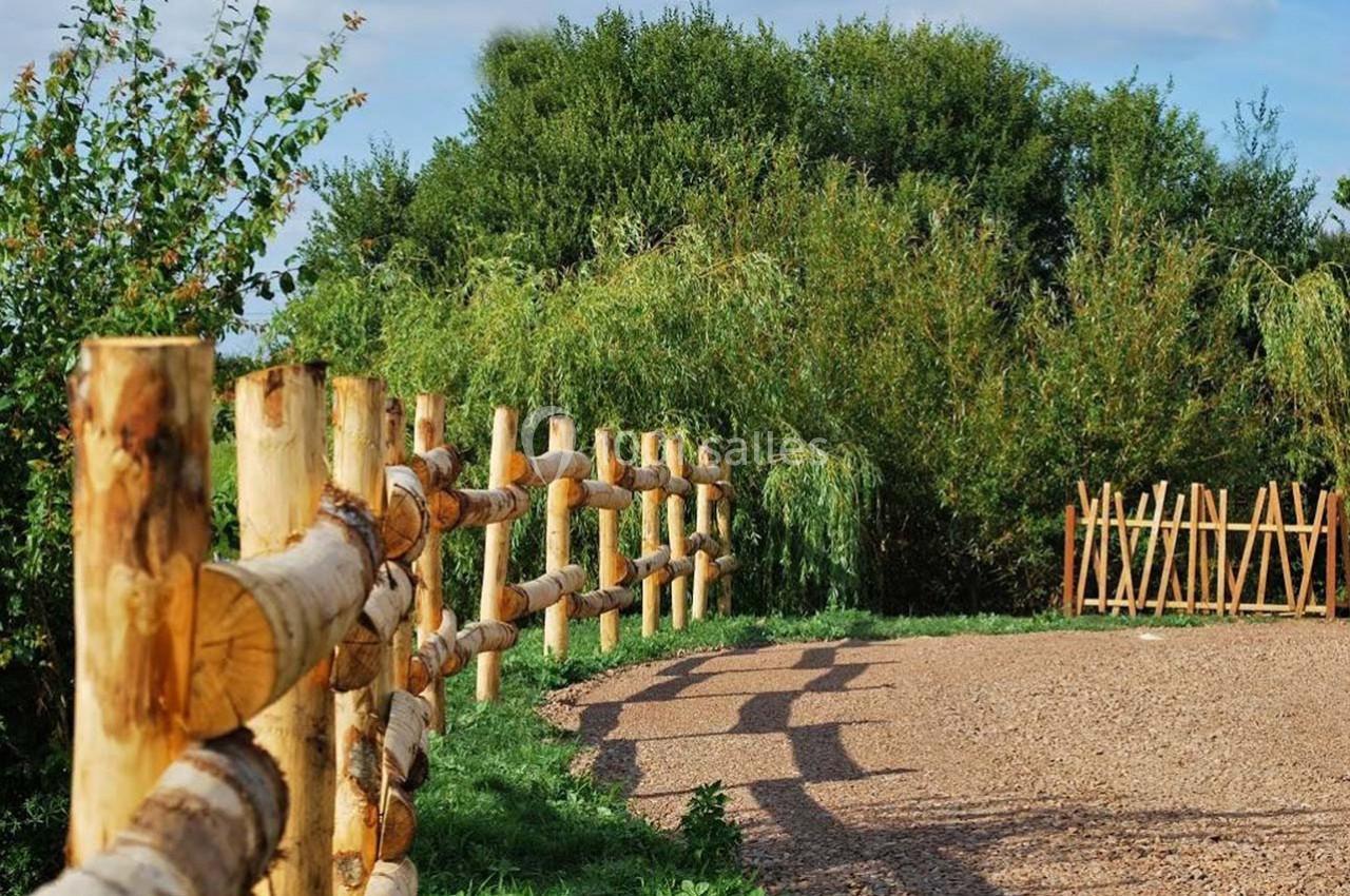 Chemin de gravier bordé d'une clôture en bois et de végétation dense sous un ciel dégagé.