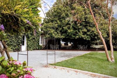 Espace salon lumineux avec fauteuils en osier, cheminée en pierre, piano, plantes et fenêtre donnant sur un jardin.