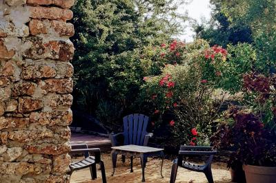 Espace salon lumineux avec fauteuils en osier, cheminée en pierre, piano, plantes et fenêtre donnant sur un jardin.