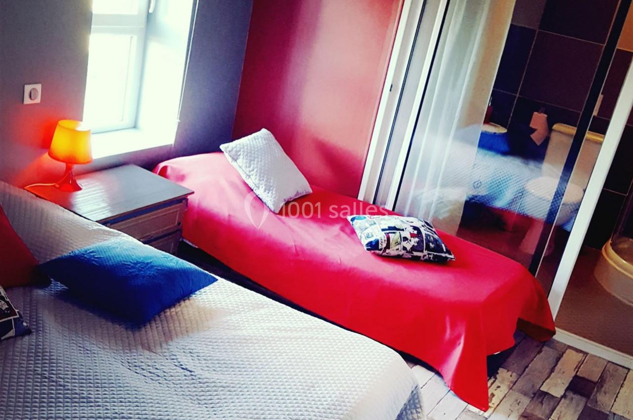 Chambre avec deux lits simples, linge coloré, lampe de chevet allumée et salle de bain attenante visible.