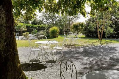 Espace salon lumineux avec fauteuils en osier, cheminée en pierre, piano, plantes et fenêtre donnant sur un jardin.