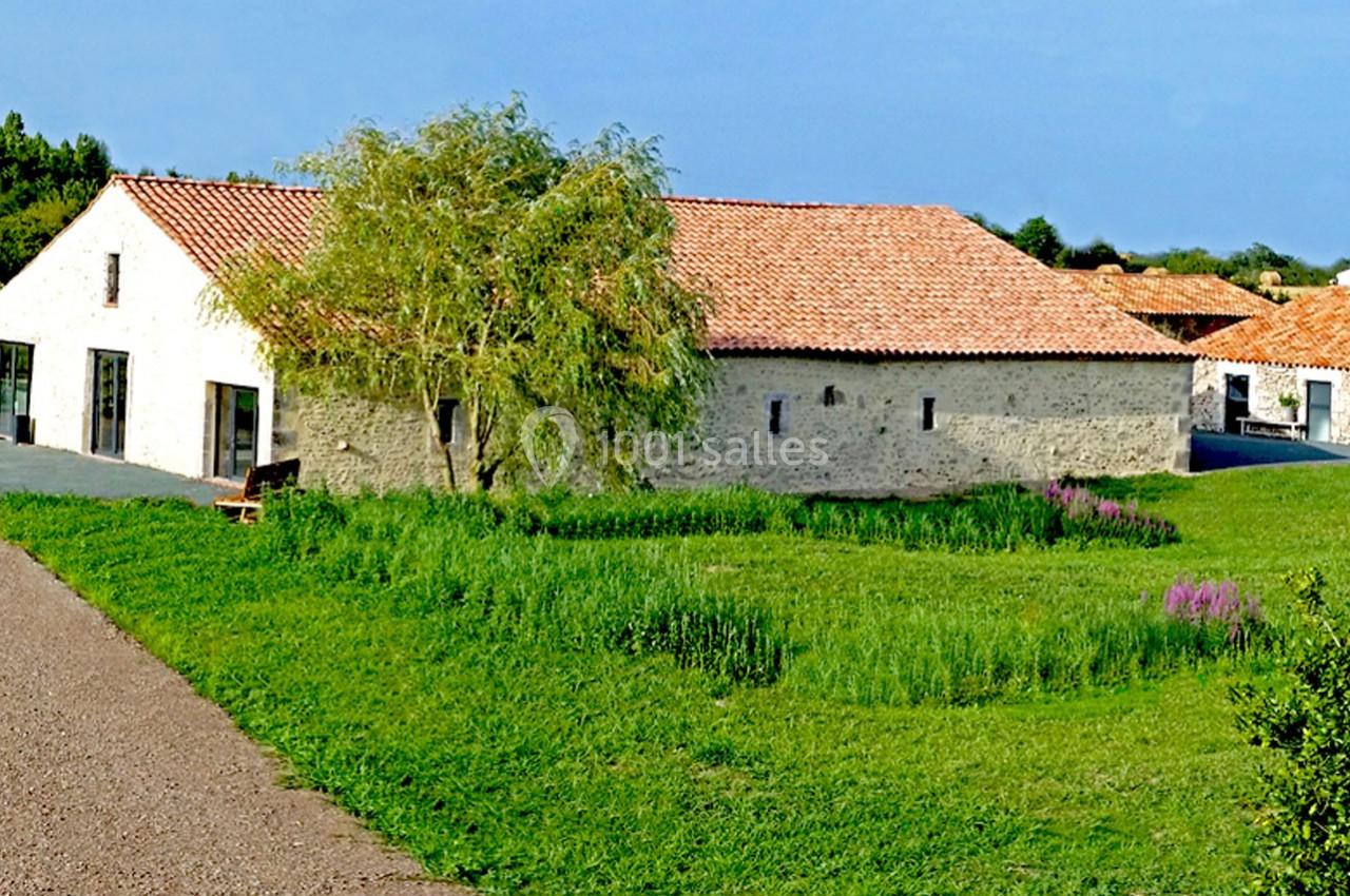 Bâtiment en pierre avec toit en tuiles rouges entouré de pelouses, d'arbustes et d'un chemin en gravier.