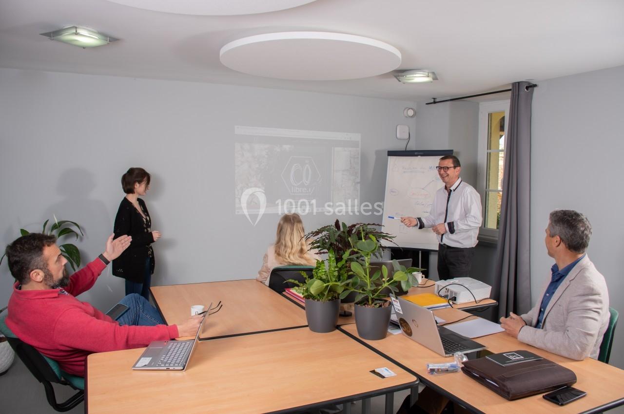 Un groupe de personnes en réunion dans une salle, avec un homme présentant des informations sur un tableau blanc.