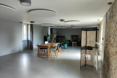 Espace salon lumineux avec fauteuils en osier, cheminée en pierre, piano, plantes et fenêtre donnant sur un jardin.