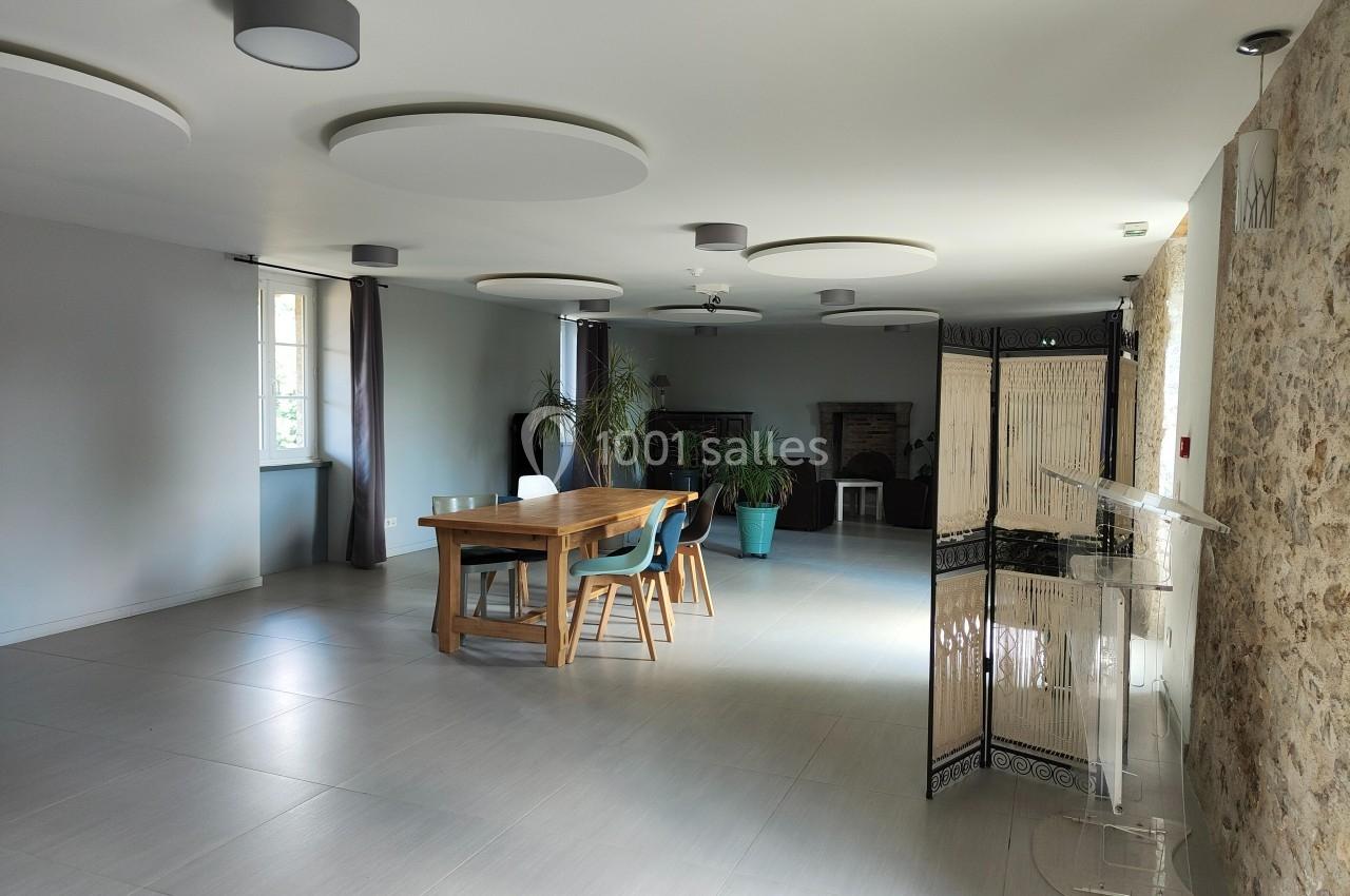 Salle lumineuse avec table en bois, chaises, plantes en pot, murs clairs et éléments en pierre apparente.