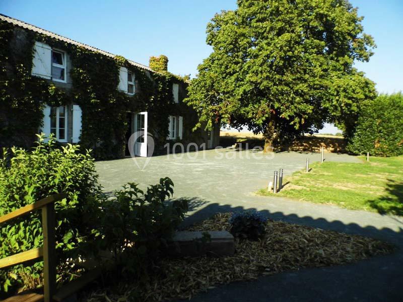 Cour d'une maison en pierre avec façade couverte de lierre, grand arbre ombrageant une partie de l'espace extérieur.