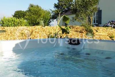 Espace salon lumineux avec fauteuils en osier, cheminée en pierre, piano, plantes et fenêtre donnant sur un jardin.