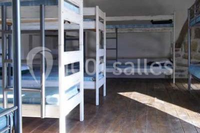 Espace salon lumineux avec fauteuils en osier, cheminée en pierre, piano, plantes et fenêtre donnant sur un jardin.