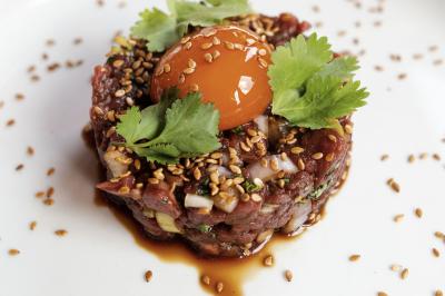 Une femme en tenue noire porte deux plateaux de hors-d'œuvre devant une porte rouge ouverte.