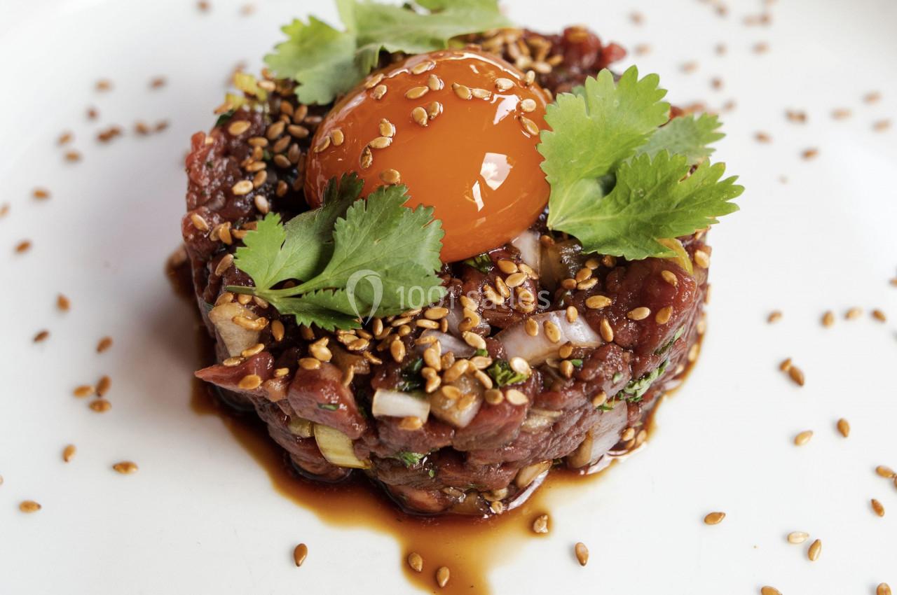 Tartare de bœuf garni de coriandre, jaune d'œuf et graines de sésame, présenté sur une assiette blanche.