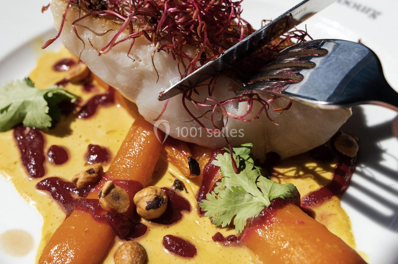 Filet de poisson avec carottes rôties, noisettes, sauce crémeuse et germes rouges, servi dans une assiette blanche.