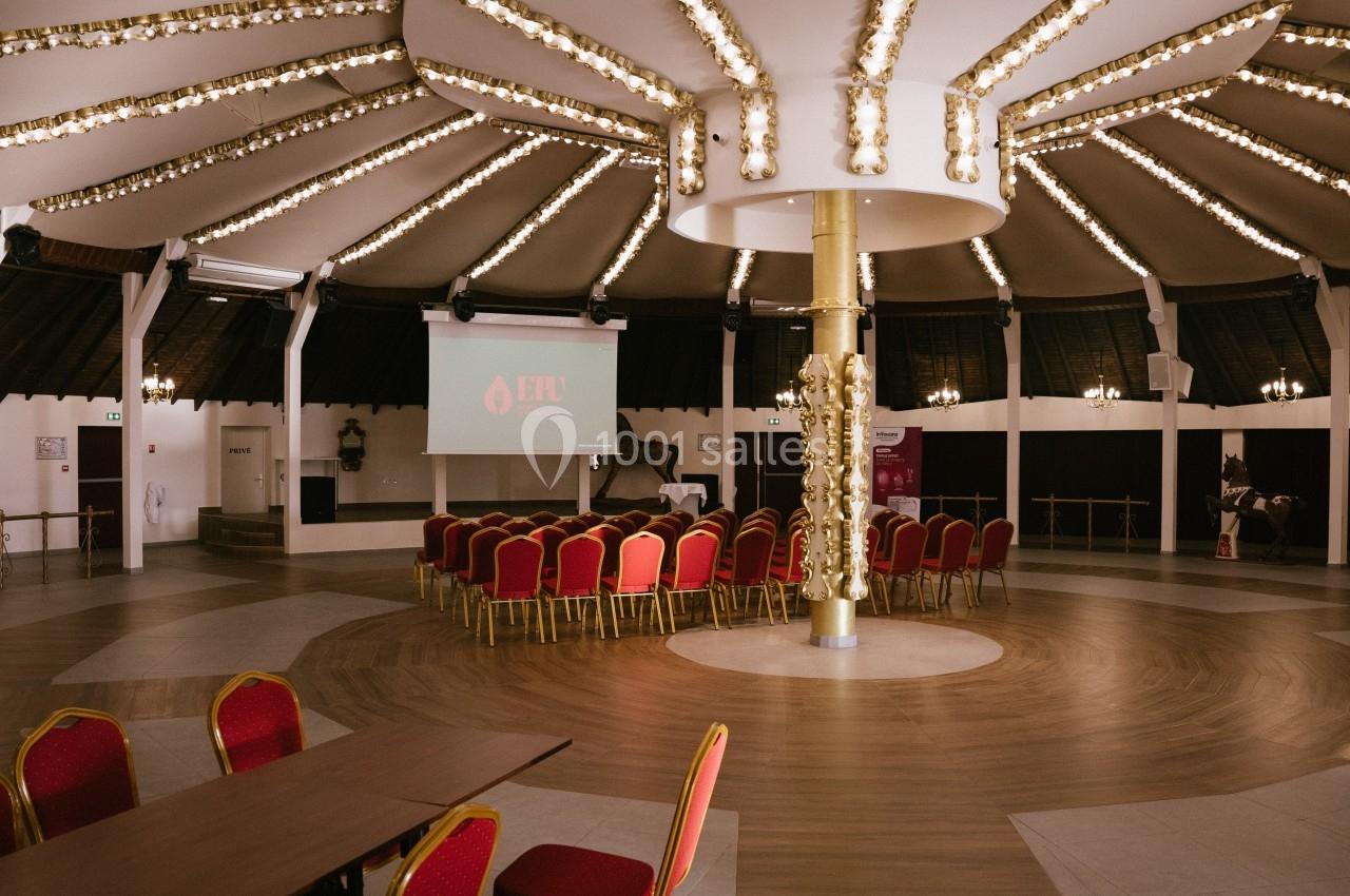 Salle circulaire avec des chaises rouges disposées devant un écran de projection, sous un plafond décoré de lumières.