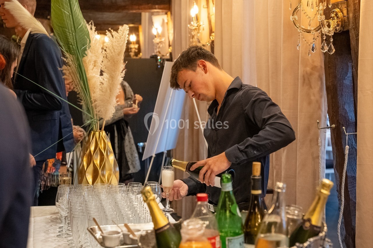 Un serveur verse du champagne dans un verre sur un bar, entouré de bouteilles et de décorations élégantes.