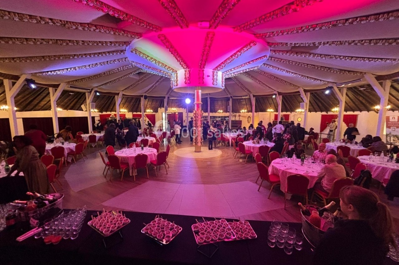 Salle circulaire décorée avec des lumières roses, tables dressées et invités rassemblés pour un événement.