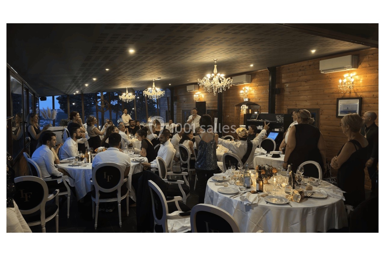 Salle de réception avec des invités assis à des tables rondes, décorée de lustres et éclairée par une lumière chaleureuse.