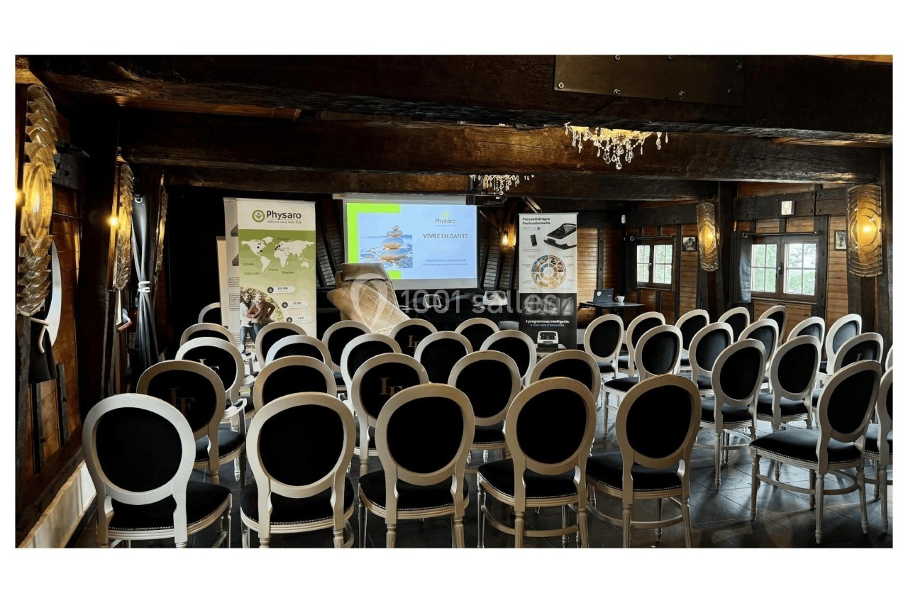 Salle de conférence avec des chaises alignées face à un écran de projection et des affiches promotionnelles.