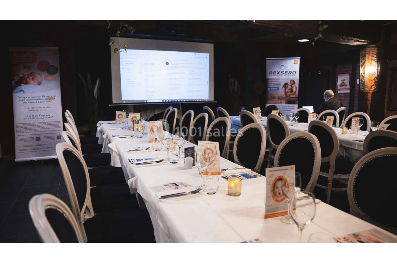 Salle de réunion avec tables dressées, documents promotionnels et écran de présentation en arrière-plan.