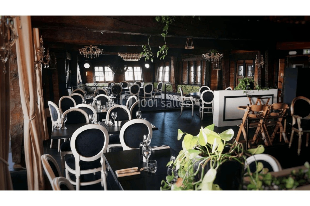 Salle de restaurant élégante avec des chaises noires et blanches, tables dressées et plantes décoratives.
