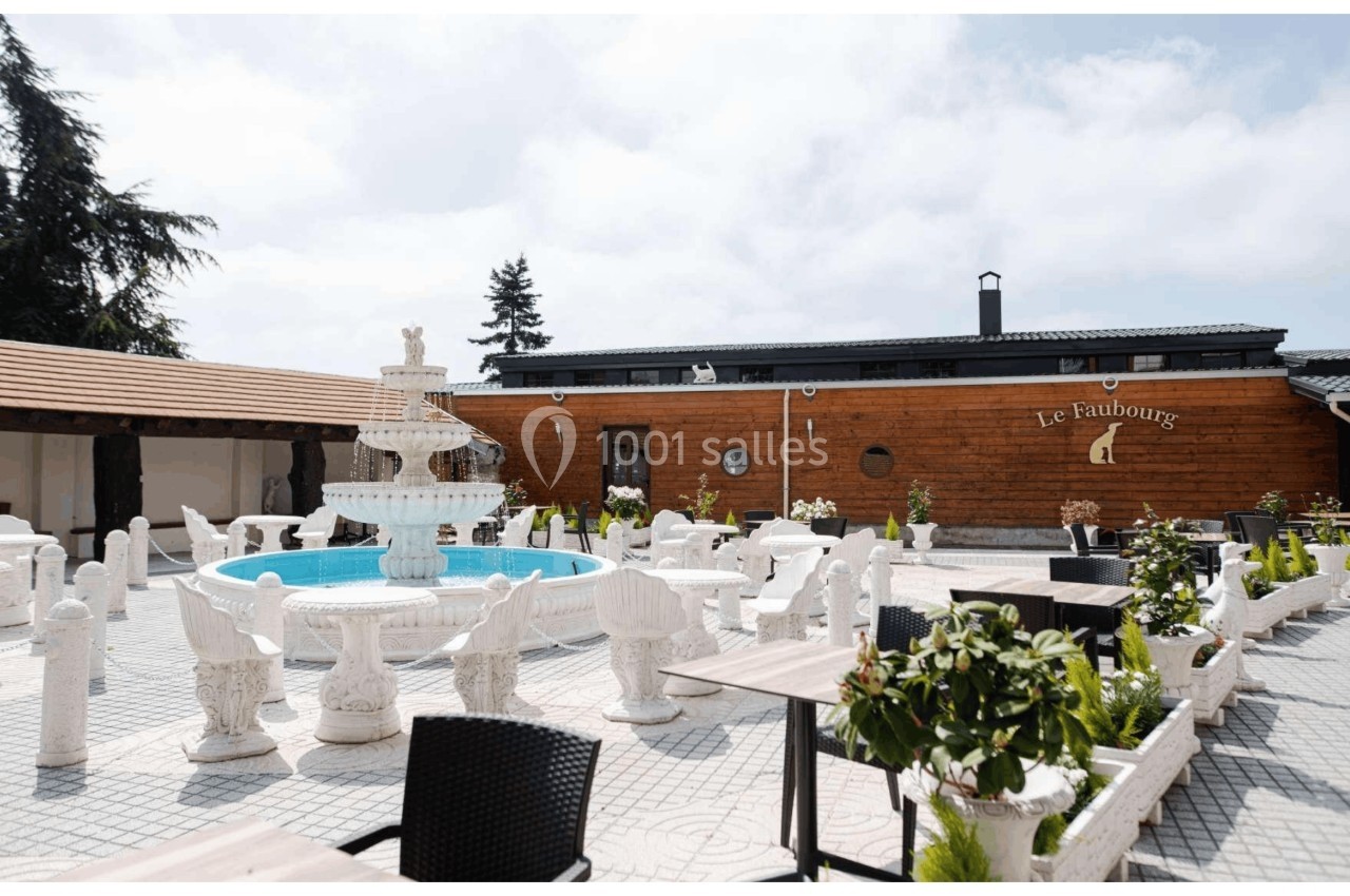 Cour extérieure avec une fontaine centrale, mobilier en pierre sculptée et bâtiment en bois en arrière-plan.