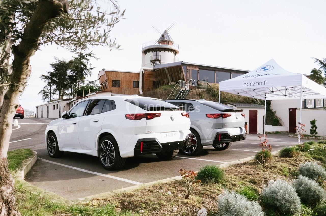 Deux voitures blanches stationnées devant un bâtiment moderne avec un moulin et une tente blanche.