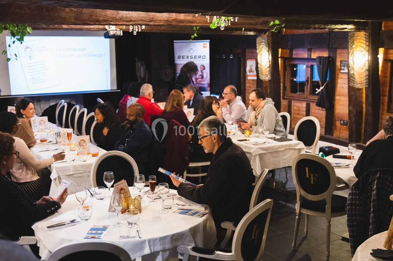 Des personnes assises autour de tables rondes dans une salle de réunion, échangeant et consultant des documents.