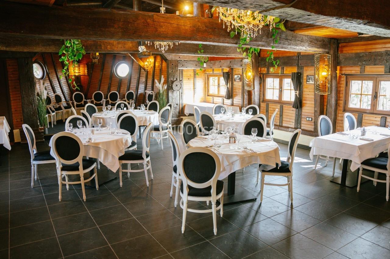 Salle de restaurant lumineuse avec des tables dressées, des chaises élégantes et une décoration rustique en bois.