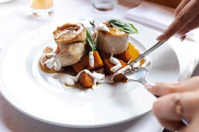 Personne coupant un plat composé de médaillons de viande, légumes rôtis et sauce blanche, servi sur une assiette blanche.