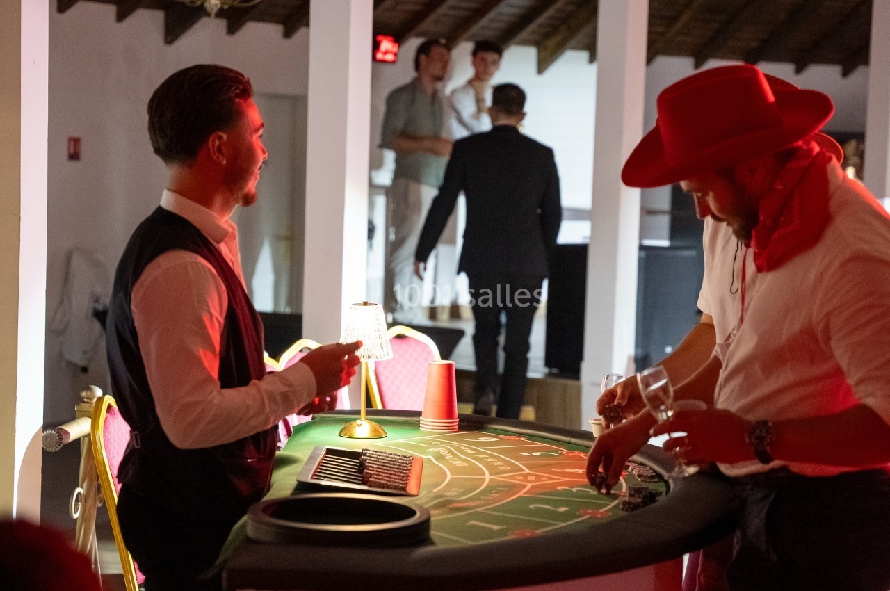 Un homme en costume anime une table de jeu de casino, tandis qu'un autre joueur mise des jetons.
