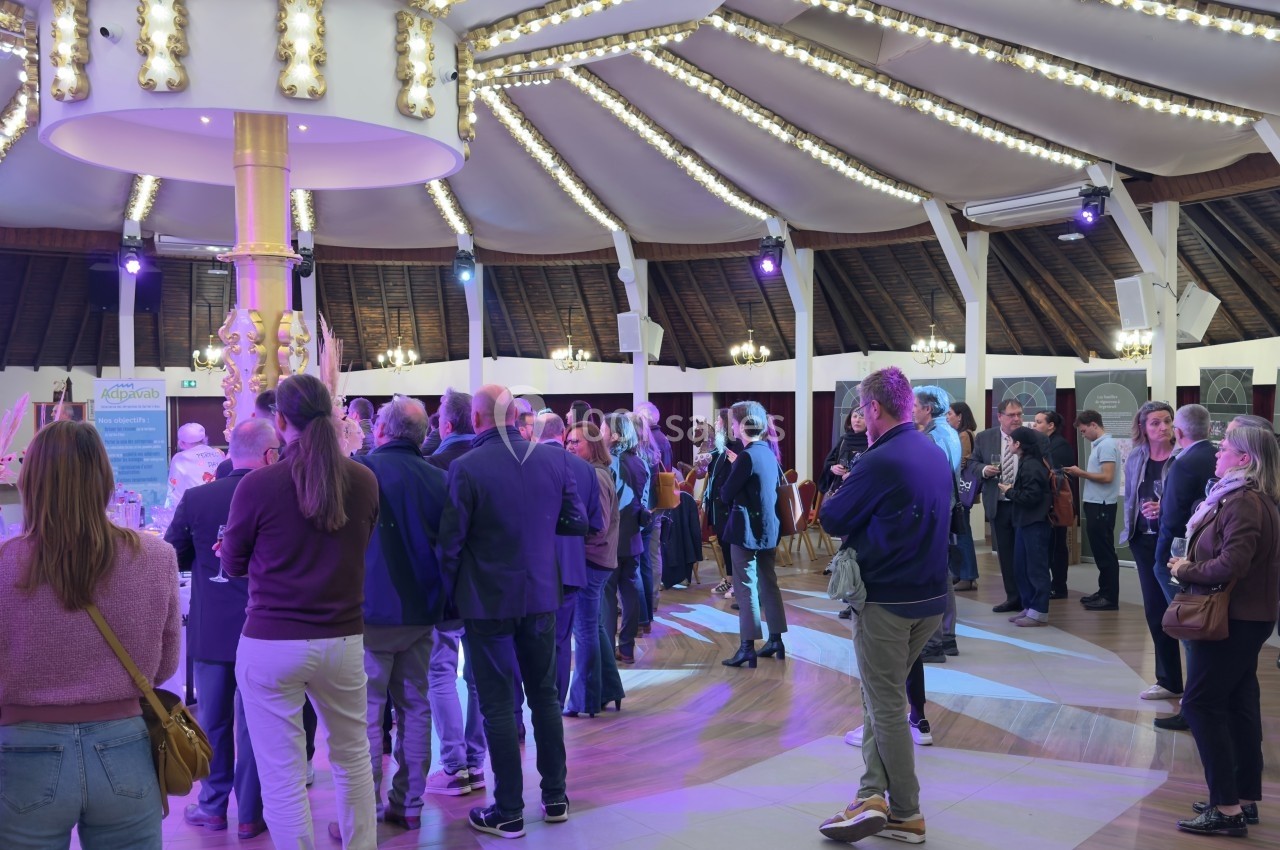 Des personnes rassemblées dans une salle circulaire éclairée, discutant debout près de stands d'exposition.