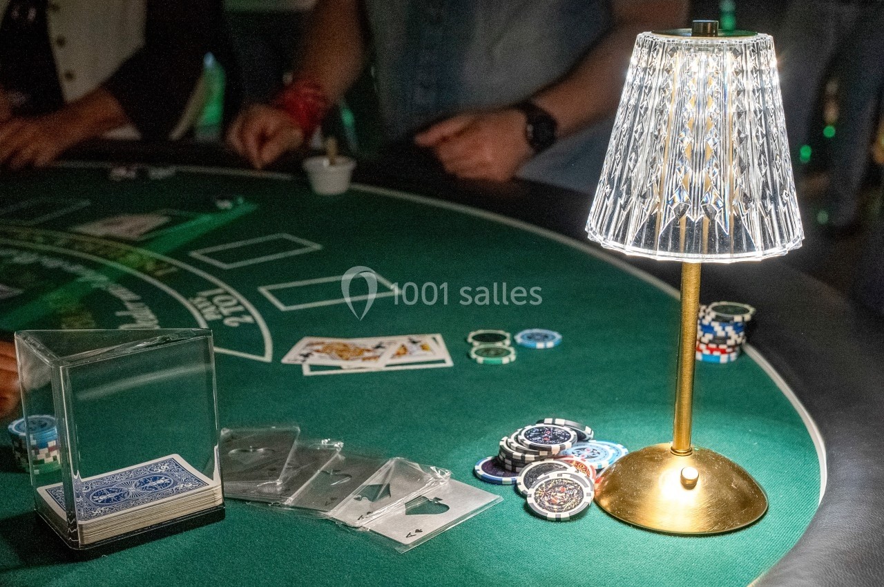 Table de jeu de casino avec des cartes, des jetons et une lampe éclairant la scène.
