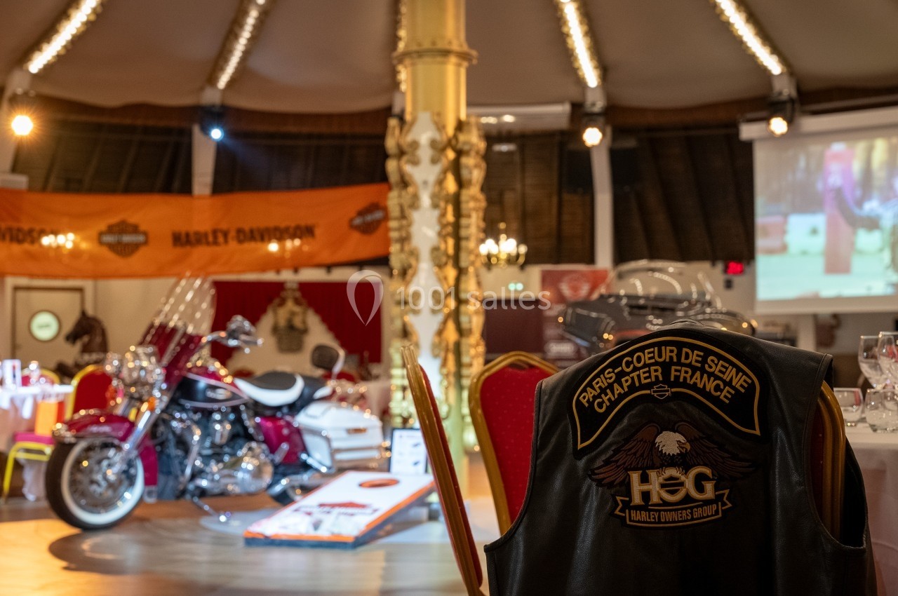 Salle décorée avec des éléments Harley-Davidson, une moto exposée et un gilet de motard posé sur une chaise.