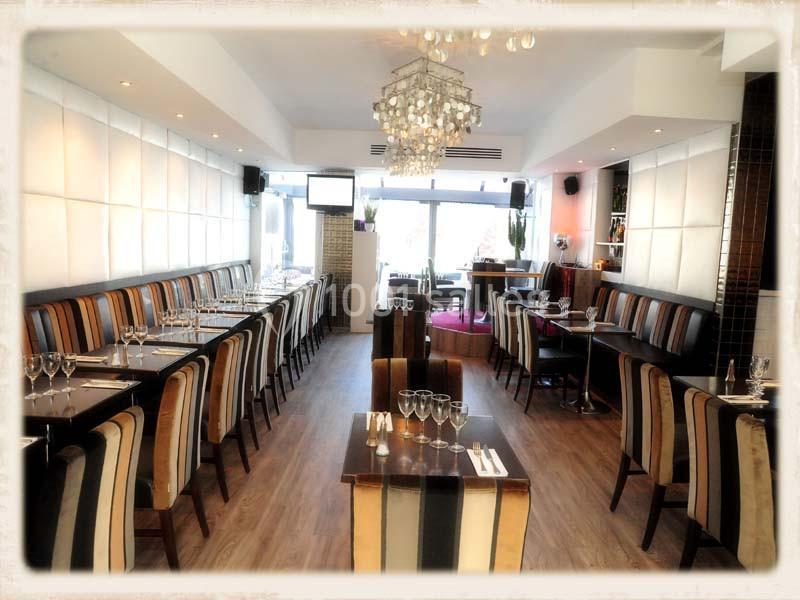 Salle de restaurant lumineuse avec tables dressées, chaises rayées et lustre central, ambiance moderne et épurée.