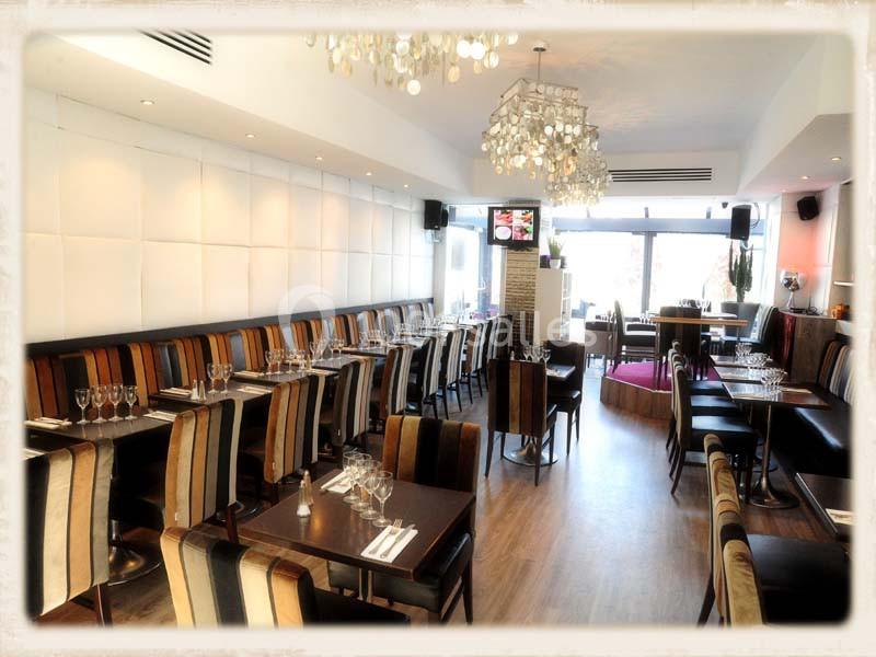 Salle de restaurant lumineuse avec tables dressées, chaises rayées et lustres modernes.